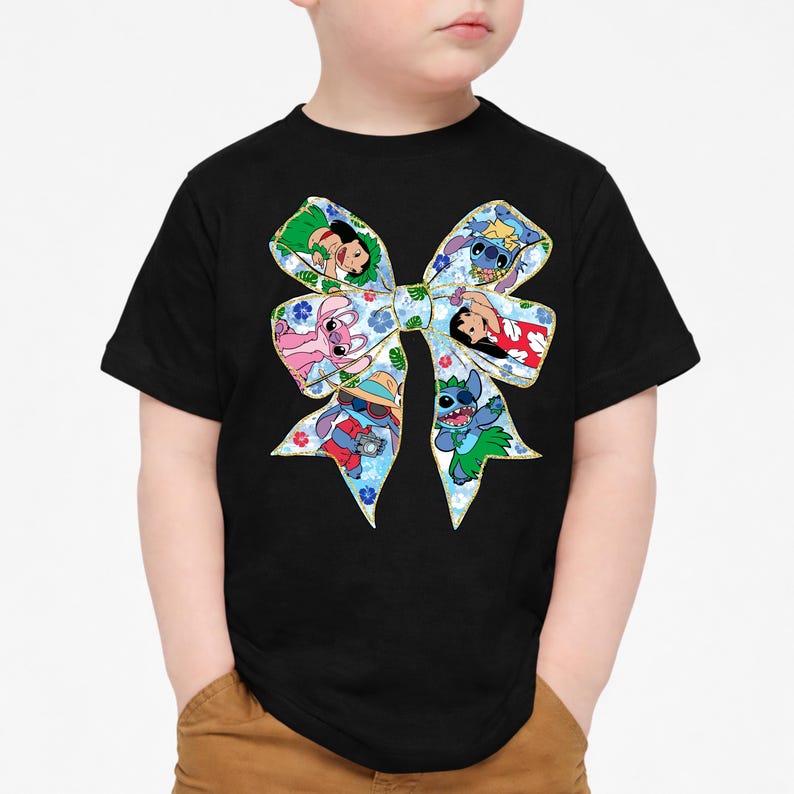 May include: Black t-shirt with a large, colourful bow design. The bow features cartoon characters on a blue floral background, with a gold outline. A fun and vibrant design.