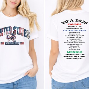 Peut inclure: T-shirt blanc avec l'inscription "UNITED STATES" dans un design patriotique et "WORLD CUP 2026". Le dos liste les villes h&ocirc;tes de la Coupe du Monde de la FIFA 2026 au Canada, aux &Eacute;tats-Unis et au Mexique.