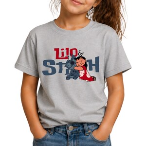 K&ouml;nnte beinhalten: Ein graumeliertes Kurzarm-T-Shirt mit einer Grafik der Figuren Lilo und Stitch, die sich umarmen. Der Schriftzug Lilo & Stitch ist in Rot und Dunkelblau auf der Brust aufgedruckt. Das T-Shirt hat einen Rundhalsausschnitt und eine normale Passform.