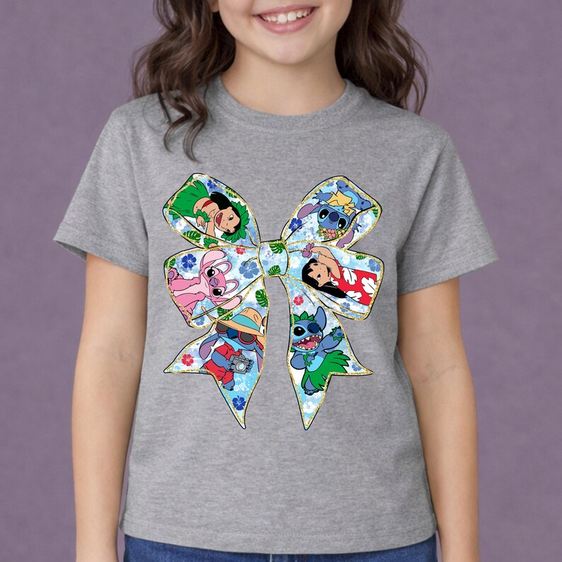 May include: A grey t-shirt with a large bow design featuring cartoon characters. The bow has a floral pattern and images of Stitch and other characters. The shirt is a short-sleeved crew neck.