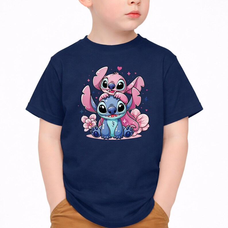 Pode incluir: Camiseta azul marinho com um desenho animado de dois personagens, um azul e outro rosa, com flores e cora&ccedil;&otilde;es rosa. O personagem azul est&aacute; sentado e o personagem rosa est&aacute; em cima. A camiseta &eacute; usada por uma crian&ccedil;a.