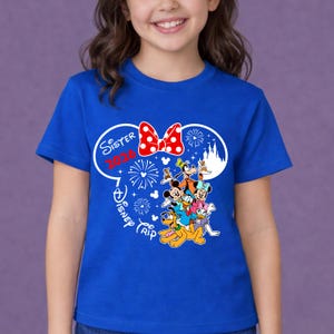 May include: A blue t-shirt featuring a graphic of Disney characters, including Mickey Mouse, Minnie Mouse, and Pluto. The design includes the text "Sister 2020 Disney Trip" in white and red, with a red bow and fireworks.