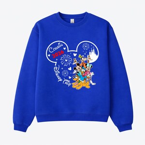 May include: Royal blue sweatshirt featuring a graphic of Mickey Mouse and friends. The design includes the text "Cousin 2026" and "Disney Trip" in a white Mickey Mouse head shape, with fireworks and a castle.