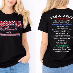 以下が含まれることがあります： 赤と白の文字で「CROATIA WORLD CUP 2026」とサッカー選手グラフィックがプリントされた黒いTシャツ。背中には、カナダ、米国、メキシコで開催されるFIFA 2026の開催都市が記載されています。