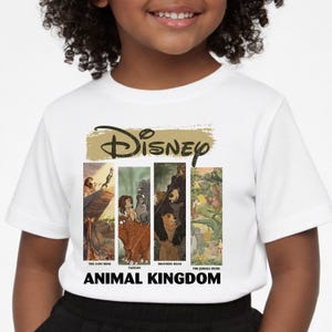Peut inclure: T-shirt blanc avec le logo Disney au-dessus de quatre panneaux illustrant des sc&egrave;nes du "Roi Lion", "Tarzan", "Fr&egrave;re des ours" et "Le Livre de la Jungle". Les mots "ANIMAL KINGDOM" sont imprim&eacute;s en dessous.