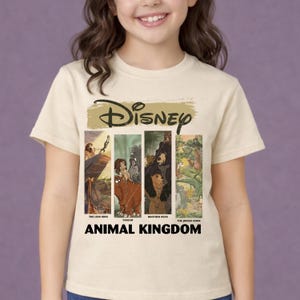 Peut inclure: T-shirt cr&egrave;me avec le logo Disney et des images de "Le Roi Lion", "Tarzan", "Fr&egrave;re des ours" et "Le Livre de la Jungle". Les mots "Animal Kingdom" sont imprim&eacute;s en noir en dessous.