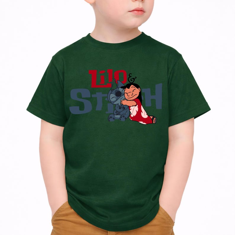 K&ouml;nnte beinhalten: Ein dunkelgr&uuml;nes Kurzarm-T-Shirt mit einer Grafik der sich umarmenden Figuren Lilo und Stitch. Der Schriftzug Lilo & Stitch ist in Rot und Blau auf der Brust aufgedruckt, wobei Lilo ein rotes Kleid mit wei&szlig;em Blumenmuster tr&auml;gt.