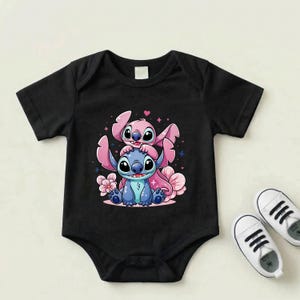 Pode incluir: Body de beb&eacute; preto com um gr&aacute;fico colorido de Stitch e Angel de Lilo & Stitch. O design inclui personagens rosa e azuis com detalhes florais. Sapatos de beb&eacute; brancos ao lado do body.