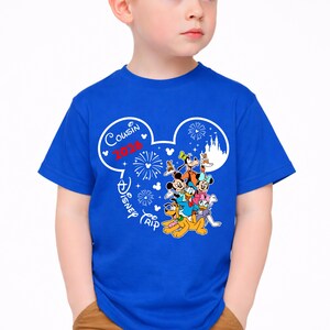 May include: A blue t-shirt featuring a white Mickey Mouse head design with the words "Cousin 2020 Disney Trip". The design includes fireworks, Disney characters, and a castle silhouette.