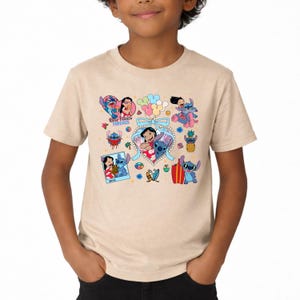 May include: A beige short-sleeve t-shirt featuring a colorful graphic print of Lilo and Stitch characters. The design includes multiple illustrations of the pair, a heart-shaped frame with a blue bow, balloons, and the text Best Friends Forever.