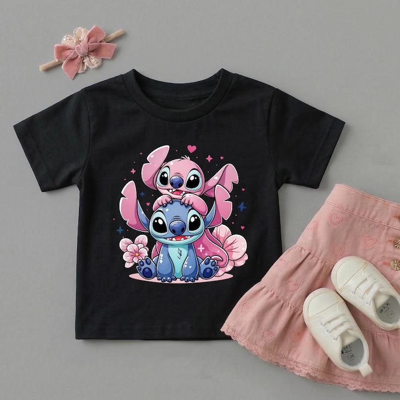 Pode incluir: Camiseta preta com uma ilustra&ccedil;&atilde;o de desenho animado de dois personagens, um azul e outro rosa, rodeados por flores e cora&ccedil;&otilde;es rosa. Uma saia rosa e sapatos brancos est&atilde;o ao lado da camiseta. Uma faixa de cabelo rosa com la&ccedil;o est&aacute; no topo.