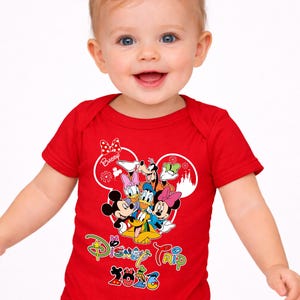 May include: A red baby bodysuit with a Disney Trip 2023 design. The graphic features Mickey Mouse, Minnie Mouse, Donald Duck, Daisy Duck, Goofy, and Pluto. The word "Baby" is written above the characters.