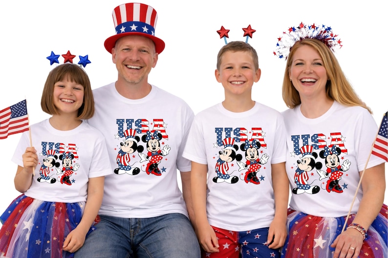 May include: A family wearing matching white t-shirts featuring Mickey and Minnie Mouse in patriotic outfits. The shirts display the word "USA" in red, white, and blue. Some family members are wearing patriotic accessories and holding American flags.