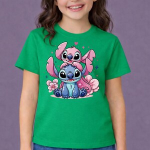 Pode incluir: Camiseta verde com uma ilustra&ccedil;&atilde;o de desenho animado de dois personagens, um azul e um rosa, com olhos e orelhas grandes. Flores e cora&ccedil;&otilde;es rosa cercam os personagens. A camiseta est&aacute; sendo usada.