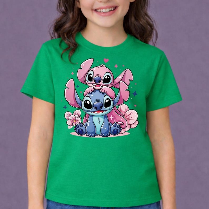 Pode incluir: Camiseta verde com uma ilustra&ccedil;&atilde;o de desenho animado de dois personagens, um azul e um rosa, com olhos e orelhas grandes. Flores e cora&ccedil;&otilde;es rosa cercam os personagens. A camiseta est&aacute; sendo usada.