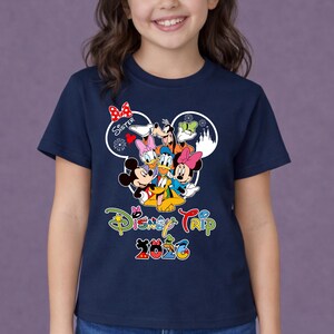 May include: A navy blue t-shirt with a vibrant Disney character design, including Mickey and Minnie Mouse, Donald Duck, and Goofy. The shirt displays "Disney Trip 2026" in a fun font, with the word "Sister" above the characters.