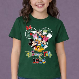 May include: Dark green t-shirt with a Disney character graphic, including Mickey and Minnie Mouse, Donald Duck, and Goofy. The shirt has the text "Disney Trip 2026" and the word "Sister".