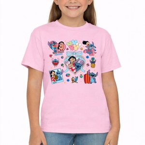 May include: A light pink short-sleeved t-shirt featuring a colorful graphic print of Lilo and Stitch characters. The design includes multiple illustrations of the pair, a heart-shaped frame, balloons, a pineapple, and the text Best Friends Forever.