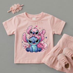 Pode incluir: Uma camiseta rosa claro com uma ilustra&ccedil;&atilde;o de desenho animado de dois personagens, um azul e um rosa, com olhos e orelhas grandes. A camisa &eacute; combinada com uma saia, sapatos e um la&ccedil;o rosa combinando.