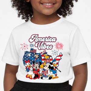 May include: White t-shirt featuring the text "America Vibes" with cartoon characters in patriotic attire. The design includes fireworks, a map of the United States, and the American flag. A fun and festive design for Independence Day.