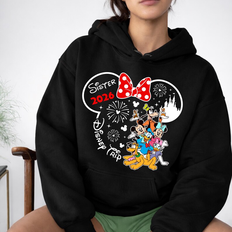 May include: Black hooded sweatshirt featuring a graphic of Disney characters, including Mickey Mouse, Minnie Mouse, and Donald Duck. The design includes a red bow, fireworks, and the text "Sister 2026 Disney Trip."