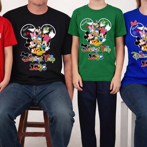 May include: Four people wearing matching t-shirts with a Disney theme. The shirts are red, black, green, and blue. Each shirt features a Mickey Mouse head design with Disney characters and the text "Disney Trip 2023".