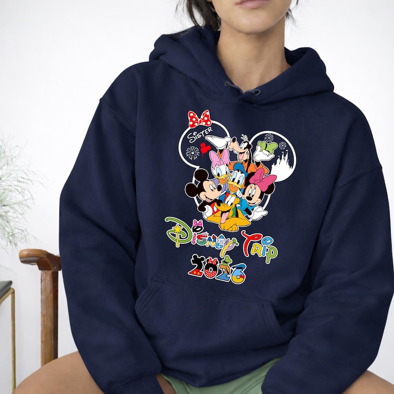 May include: Navy blue hooded sweatshirt with a vibrant graphic of Disney characters, such as Mickey and Minnie Mouse, Donald and Daisy Duck, and Goofy. The text "Disney Trip 2023" is printed below the characters. A red bow is above the word "Sister".
