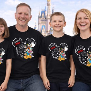 May include: Four people wearing matching black t-shirts with a Mickey Mouse head design. Each shirt has a different title: "Sister", "Daddy", "Cousin", and "Mommy", with "2026" and "Disney Trip" text. The background shows a theme park.