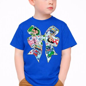 May include: A blue t-shirt with a large bow design featuring cartoon characters. The bow is decorated with floral patterns and images of characters in various poses. The shirt is made of a soft material.