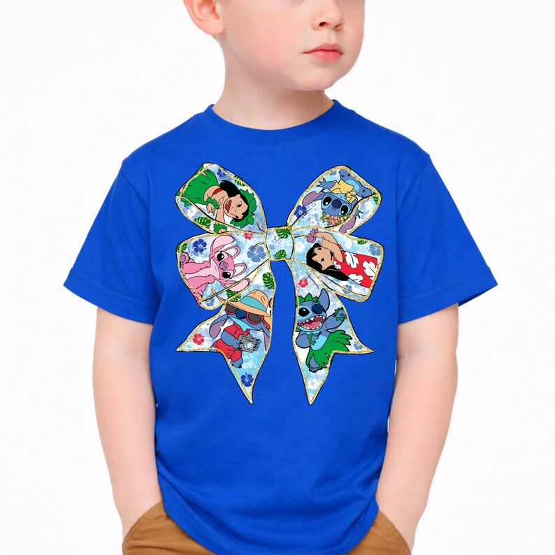 May include: A blue t-shirt with a large bow design featuring cartoon characters. The bow is decorated with floral patterns and images of characters in various poses. The shirt is made of a soft material.