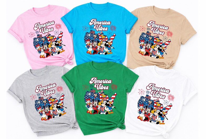 May include: A collection of six t-shirts in various colors: pink, blue, tan, gray, green, and white. Each shirt features the text "America Vibes" above a graphic of cartoon characters in patriotic attire, set against a map of the United States.
