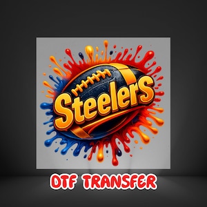 May include: A digital graphic of a football with the word "Steelers" in bold, orange letters. The football is navy blue and gold, with orange and red paint splatters surrounding it. The text "DTF TRANSFER" is at the bottom.