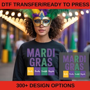 May include: Black sweatshirt with the text "MARDI GRAS" in purple and green, with the words "Beads, Parades, Crawfish, Kingcake" below. The image also includes a mask and the text "DTF TRANSFER/READY TO PRESS" and "300+ DESIGN OPTIONS".