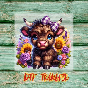 Op de afbeelding: Een digitale DTF-transfer met een cartoon Highland-kalf met een paarse ruitjesstrik, omringd door zonnebloemen, rozen en andere bloemen. Het kalf heeft grote blauwe ogen en een roze neus. De tekst "DTF TRANSFER" is in oranje.