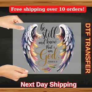 Peut inclure: Un motif de transfert numérique représentant une paire d'ailes d'ange colorées avec le texte "Be still and know that I am God. Psalm 46:10".