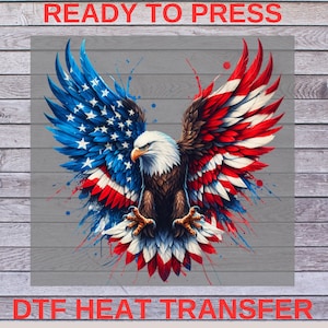 May include: A bald eagle with its wings spread wide, forming the shape of the American flag. The eagle is in a vibrant red, white, and blue color scheme with paint splatters around it. The text "READY TO PRESS" is at the top of the image, and "DTG HEAT TRANSFER" is at the bottom.