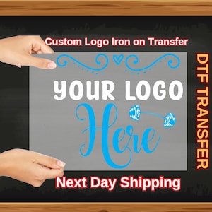 May include: A gray iron-on transfer sheet with the text "Your Logo Here" in white and blue lettering. The text is surrounded by a decorative design of swirls and hearts. The text "DTG Transfer" is written vertically on the right side of the sheet. The text "Custom Logo Iron on Transfer" is written at the top of the sheet. The text "Next Day Shipping" is written at the bottom of the sheet.