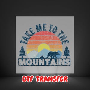 May include: A distressed graphic with the text "TAKE ME TO THE MOUNTAINS" above a mountain scene with a bear silhouette, trees, and a sunset. The words "DTF TRANSFER" are at the bottom.
