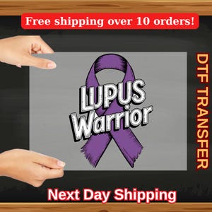 May include: A purple ribbon with the words "LUPUS Warrior" in a bold, outlined font. The design is on a gray background, with the words "DTF TRANSFER" in orange on the right side. The words "Next Day Shipping" are at the bottom.