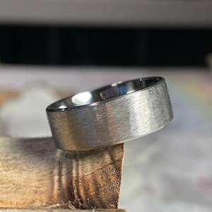 May include: A brushed silver wedding band with a flat, wide profile.