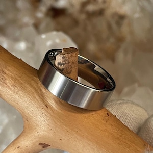 May include: A silver-toned metal ring with a smooth, polished finish and a flat band profile. The ring features a simple, unadorned design with a reflective surface that catches light, showcasing a clean and uniform circular shape throughout the band.