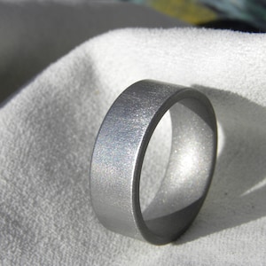 May include: A silver-colored metal ring with a brushed finish. The ring is thick and has a rounded edge.