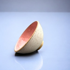 Könnte beinhalten: Eine Keramikschale mit gesprenkeltem Äußeren und rosa Innenraum. Die Schale hat eine hellbeige Farbe mit kleinen braunen Sprenkeln. Der Innenraum ist zartrosa. Die Schale hat einen kleinen, abgerundeten Boden.
