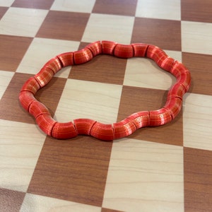 May include: A red and gold flexible toy made of connected segments, shaped into a circle, on a checkered surface.