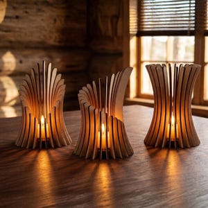 May include: Three wooden candle holders with a fan-like design, each holding a lit candle. The holders are made of light-coloured wood and sit on a dark wooden table. The warm glow of the candles creates a cosy atmosphere.
