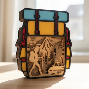 Puede incluir: Una obra de arte de madera en capas que representa una mochila con una escena de montaña. La mochila tiene un cuerpo amarillo, ribetes negros, detalles rojos y una parte superior azul. La escena de la montaña presenta excursionistas y árboles.