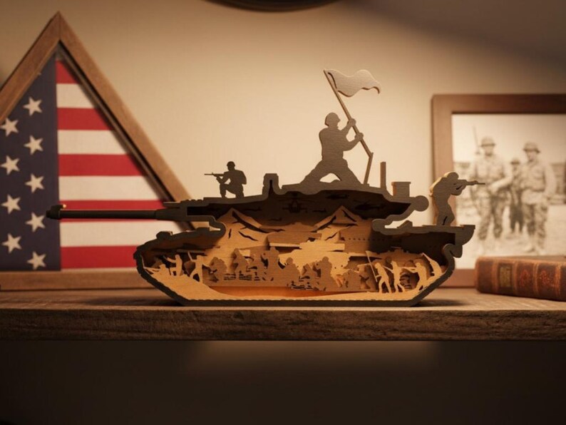 May include: A layered wooden tank sculpture with soldiers and a flag. The tank is brown with detailed cutouts depicting a battle scene. An American flag and a framed photograph are in the background.