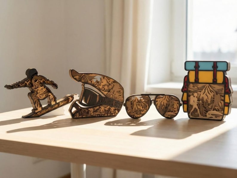 May include: Wooden decorative items including a snowboarder, a motorcycle helmet, aviator sunglasses, and a backpack. The items are made of layered wood, with intricate details. The sunglasses have a mountain scene reflected in the lenses.