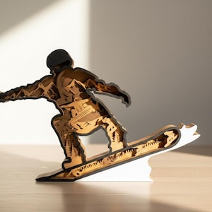 May include: A wooden sculpture of a snowboarder in motion. The figure is made of layered wood, with a black outline and a natural wood color for the body and snowboard. The base is white.