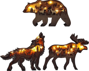 May include: Three wooden silhouette light-up decorations featuring a bear, wolf, and moose. Each silhouette is cut out and features a forest scene with trees and deer. The lights are warm white and create a cozy glow.